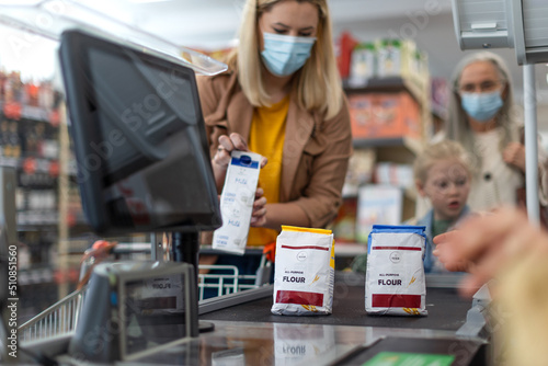 Young woman shopping in supermarket, putting products on checking desk during pandemic photo