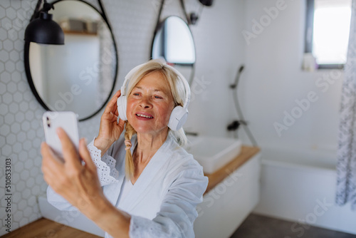 Beautiful senior woman in bathrobe listening to music in bathroom, relax and wellness concept.