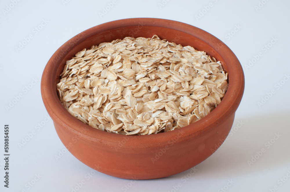 Dried oats, brown earthenware bowl full of lightly-colored oat flakes. Profile view of popular, natural and healthy breakfast meal isolated on clean white background. Dried oats, brown earthenware bowl full of lightly-colored oat flakes. Profile view of popular, natural and healthy breakfast meal isolated on clean white background.