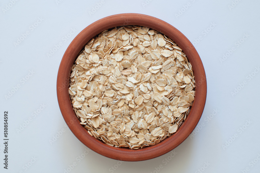 Top view of natural and raw oat flakes in brown earthenware casserole. Popular healthy oat meal isolated on white background. Top view of natural and raw oat flakes in brown earthenware casserole. Popular healthy oat meal isolated on white background.