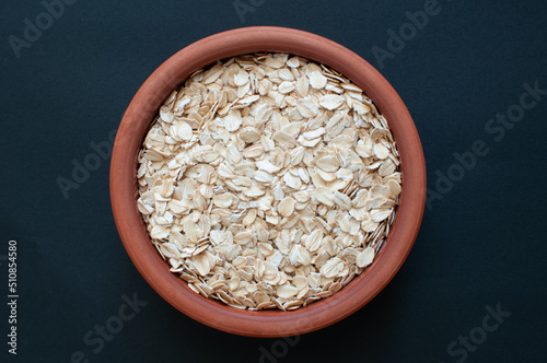Top view of organic and vegan oat flakes in earthenware casserole. Popular healthy oat meal isolated on dark background.