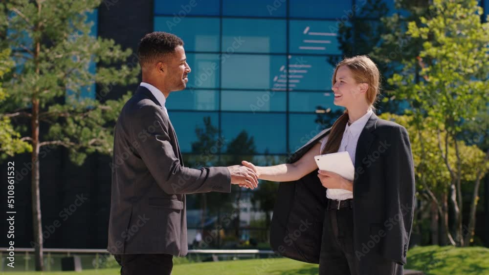 In front of modern business centre two office workers one charismatic black man and one beautiful lady have a discussing about work then shaking hands they are feeling excited In front of modern business centre two office workers one charismatic black man and one beautiful lady have a discussing about work then shaking hands they are feeling excited
