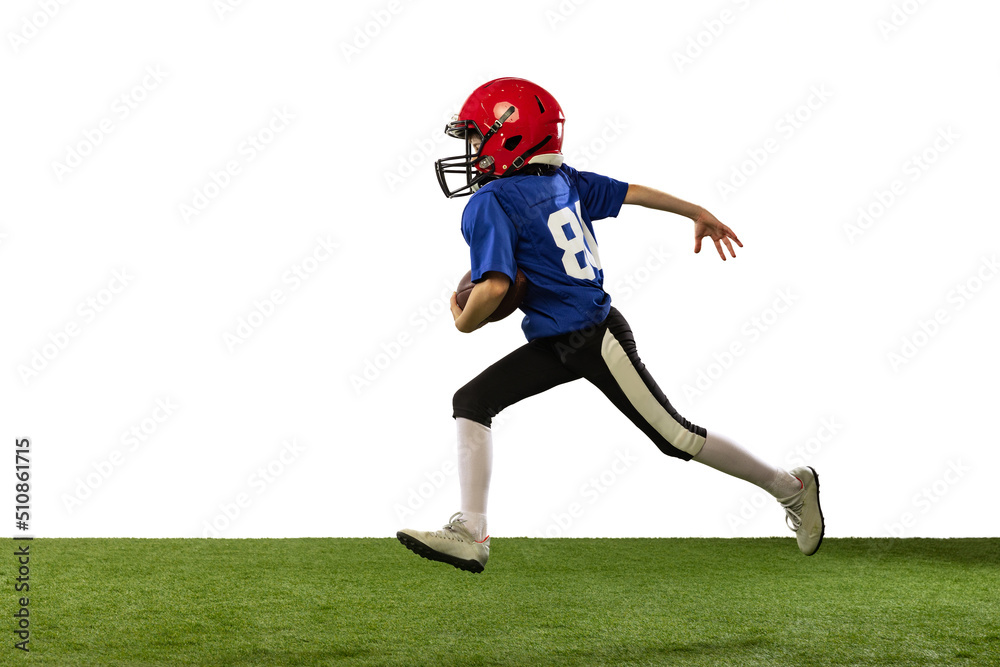 Sportive little boy in sports uniform and equipment playing american football isolated on green background in neon light. Concept of sport, movement, achievements.