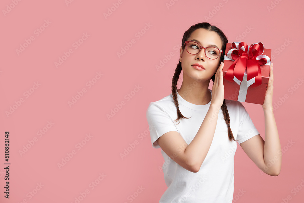Cute Asian girl is holding the gift box and standing on pink background, blank copy space for your advertising content. Cute Asian girl is holding the gift box and standing on pink background, blank copy space for your advertising content.