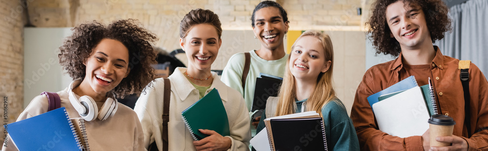 young and cheerful multiethnic students with copybooks smiling at camera, banner. young and cheerful multiethnic students with copybooks smiling at camera, banner.