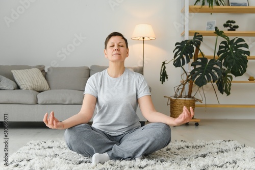 Middle-aged woman doing yoga at home for stretching and being healthy.