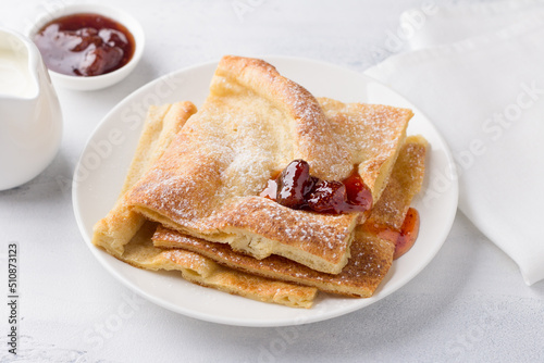 Fotografie A plate of traditional finnish or danish pancakes pannukakku sprinkled with powdered sugar with sour cream and jam on a light background
