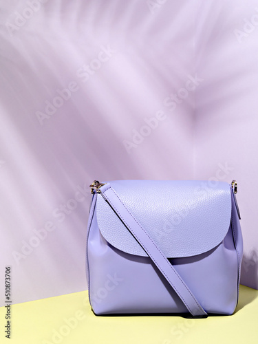 Minimalist stylish female accessory. Single trendy purple crossbody handbag with tropic leaves shadow overlay. Summer sale background with copy space. Style and minimalist fashion concept.