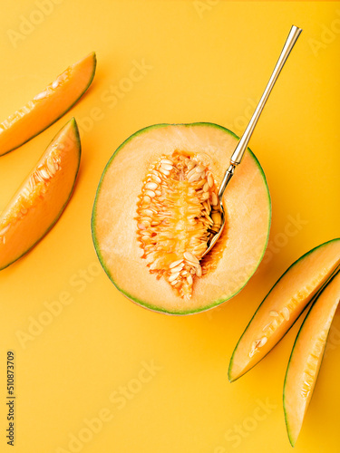 Exotic cantaloupe melon and slices on marigold coloured backdrop. Ripe tropical fruit background. Idea of summer season food trend. Food photography. Flat lay, copy space.