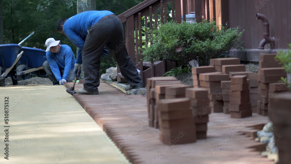 Using a rubber mallet, a hardscaper taps the red brick pavers into