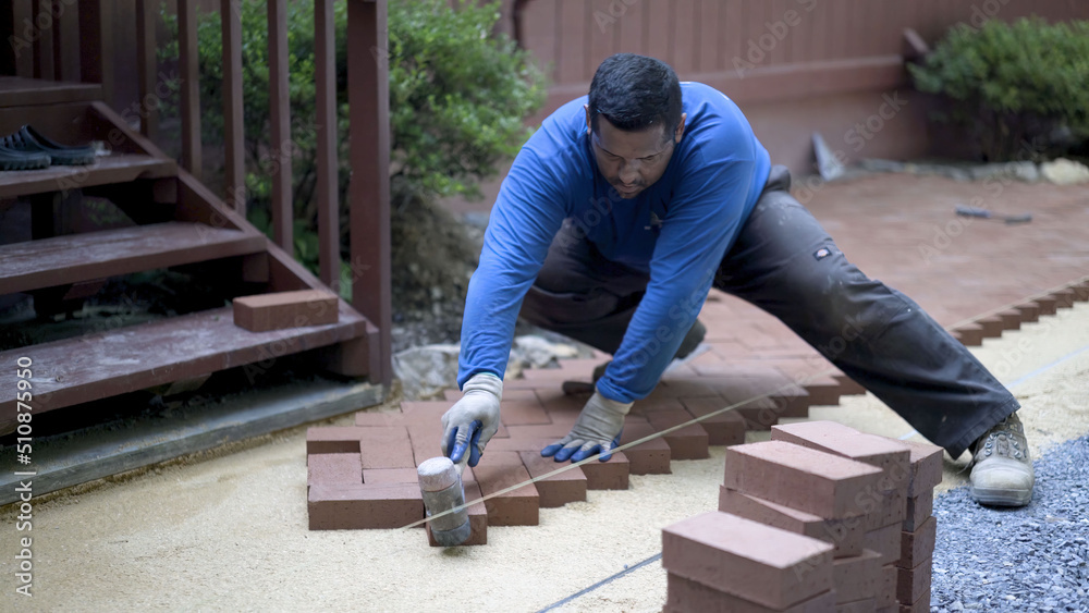 Foto de Using a rubber mallet, a hardscaper taps the red brick pavers