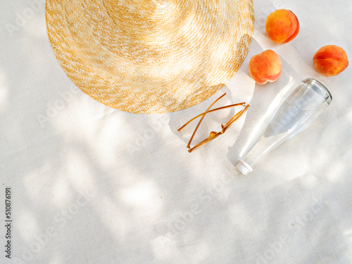 Vintage inspired background with straw hat, female sunglasses, bottle of water  and fruits on white towel. Minimalist summer vacation creative still life ​for fashion blog, web, social media, stories.