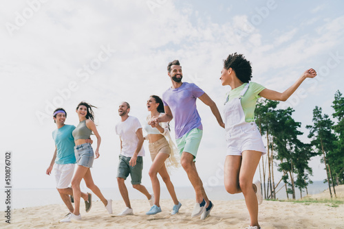 Photo of positive carefree people hold hands walk running beach coast free time hang out outside