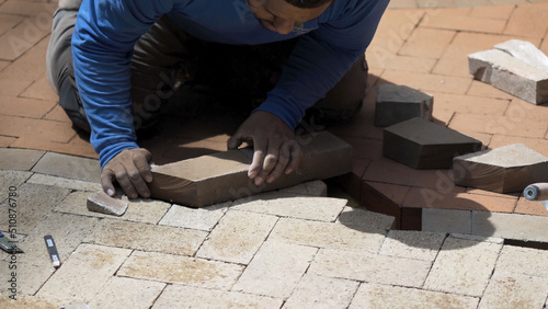 Closeup shot of man fitting a custom cut brick into a two-tone brick paver emblem design as part of a hardscaping project.