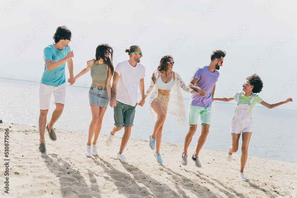 Full size photo of carefree overjoyed people hold arms running have fun chilling sand beach outdoors