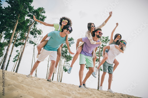 Full length photo of cheerful friendly people piggyback have fun hang out sand beach outdoors