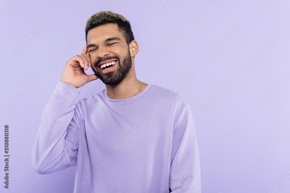 happy african american man in sweater talking on smartphone and laughing isolated on purple. happy african american man in sweater talking on smartphone and laughing isolated on purple.