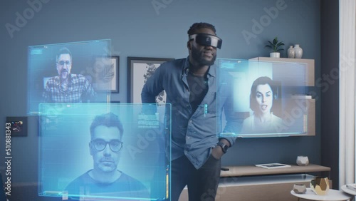Afro-american man wearing VR goggles at online business meeting in meta universe cyberspace talking with colleagues over video conference, holographic windows in front of him photo