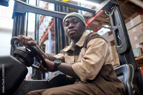 Portrait of African american driver looking at camera while driving forklift at warehouse