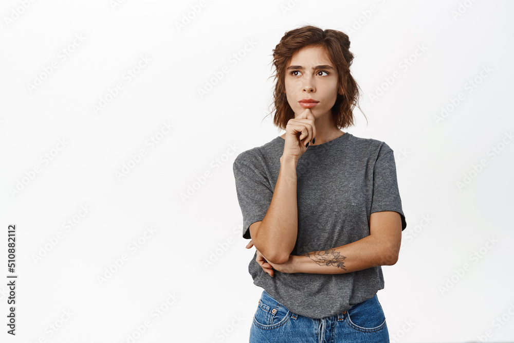 Woman with thoughtful face touching chin, thinking, making decision, standing in grey tshirt over white background Woman with thoughtful face touching chin, thinking, making decision, standing in grey tshirt over white background