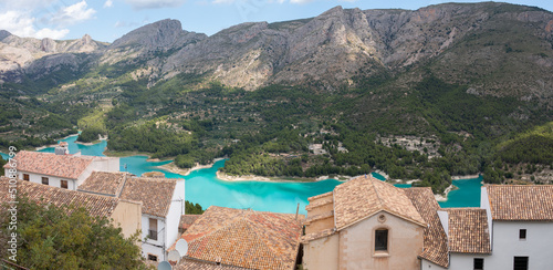 Fototapeta Naklejka Na Ścianę i Meble -  Panoramic view with the roofs of the houses of the village of Guadalest with the Serrella mountain range in the background and the Guadalest reservoir in the lower , Alicante, Spain
