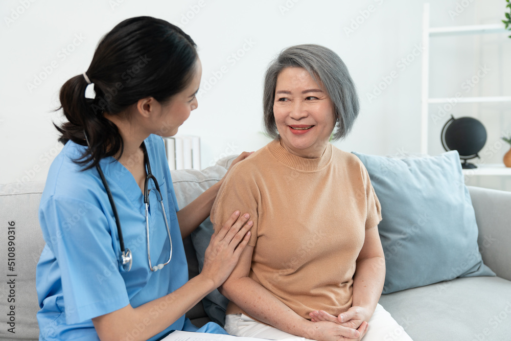 Asian young woman caregiver nurse talking with grandmother sitting on sofa in living room during home visit..Young female psychological doctor give help take care of elderly woman patients. Asian young woman caregiver nurse talking with grandmother sitting on sofa in living room during home visit..Young female psychological doctor give help take care of elderly woman patients.