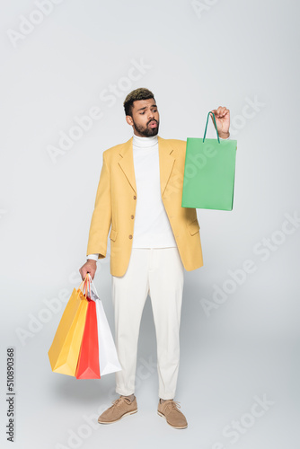 full length of african american man in yellow blazer and polo neck holding shopping bags on grey. © LIGHTFIELD STUDIOS