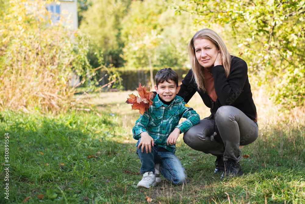 Fototapeta premium Mom picks up son from school, they come home through the park and talk, laugh, have fun together, collect autumn leaves together
