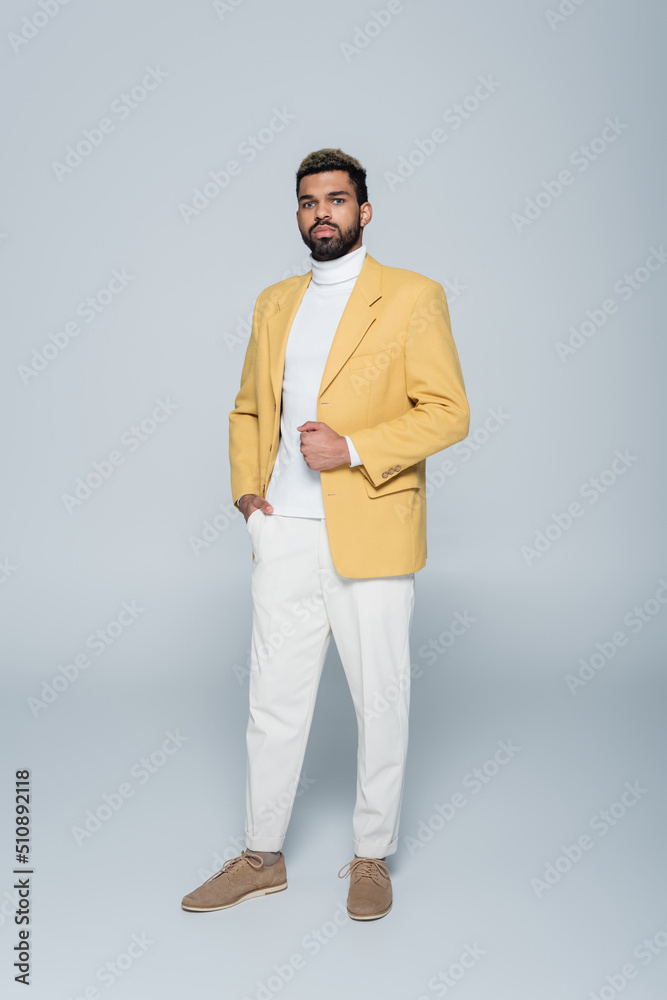 full length of stylish african american man in yellow blazer posing on grey. full length of stylish african american man in yellow blazer posing on grey.