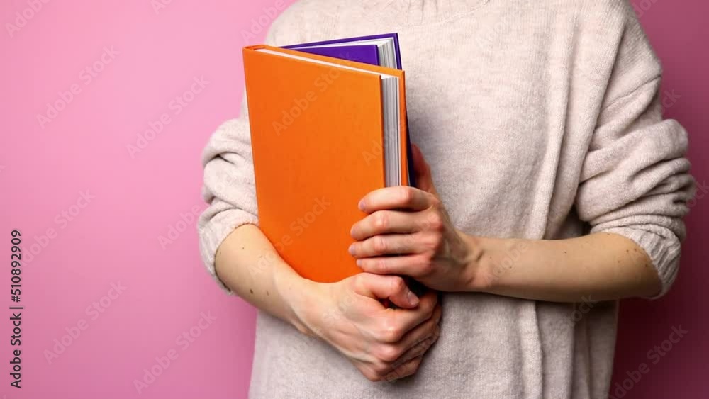 Unrecognizable woman in sweater holding books in front of pink background. Unrecognizable woman in sweater holding books in front of pink background.