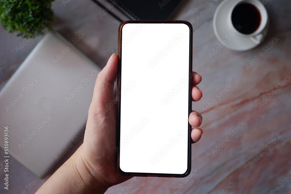 Mockup picture of business woman’s hands holding smart phone with white blank screen in modern place