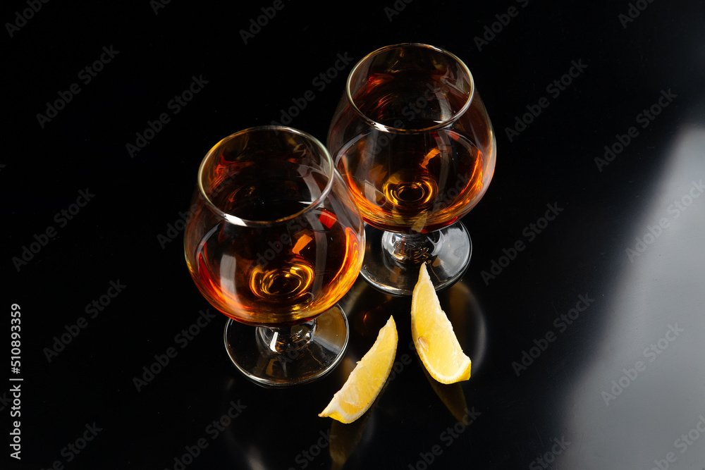 Two glasses with brandy and lemon. On a black background.