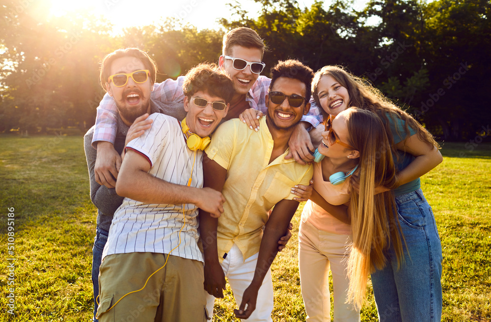 Portrait of happy diverse friends having fun on warm sunny evening in summer park. Bunch of cheerful young people standing on green lawn, smiling and posing for funny group photo together - obrazy, fototapety, plakaty 