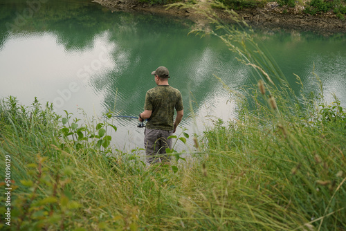 A man in shorts, a green T-shirt and a cap is fishing in a blue river