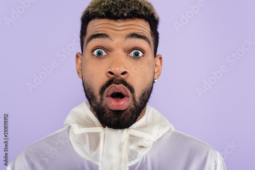 portrait of shocked african american man with blue eyes isolated on purple.