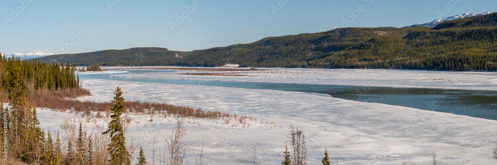 Spring time panoramic view in northern Canada with snow capped mountains over the Yukon River. 