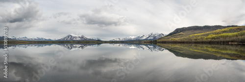 Panoramic view of a wilderness lake in Canada during spring with reflection of snow capped mountains in water. 