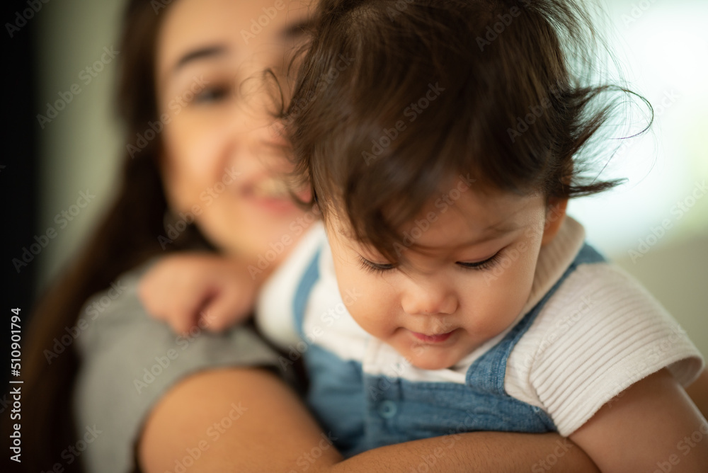 Cute little baby toddler pouncing and jumping while in the arms of young mother hugging at home Cute little baby toddler pouncing and jumping while in the arms of young mother hugging at home