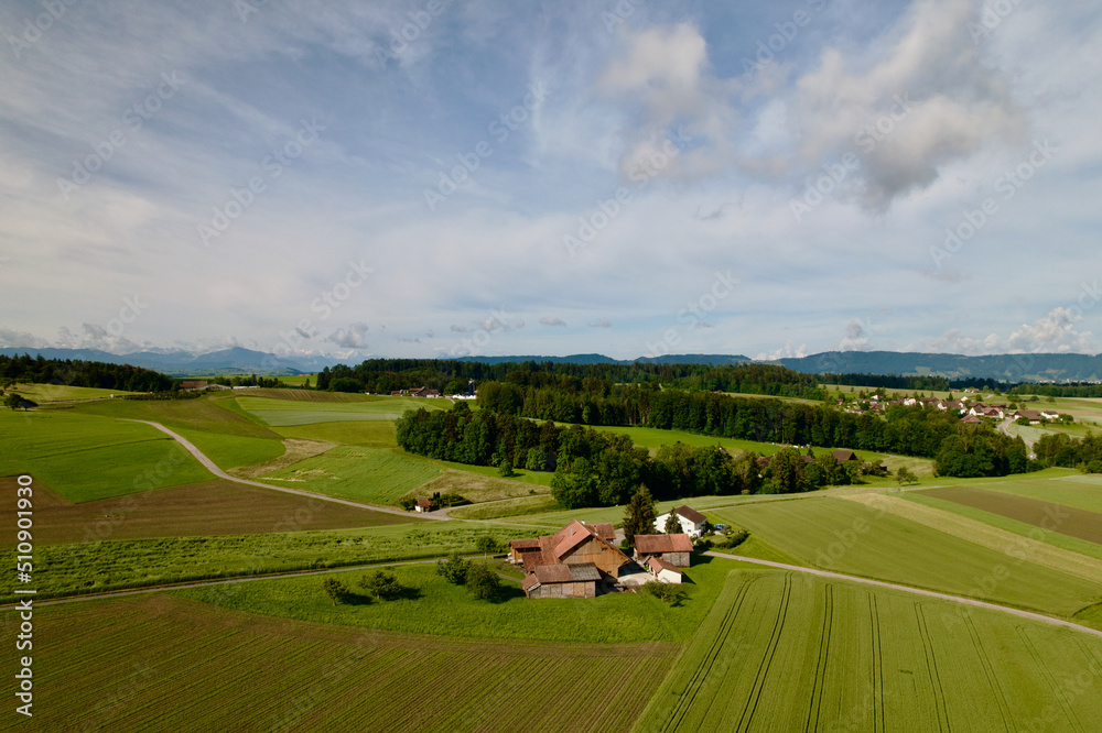 Aerial view of agricultural landscape with farm houses and cloudy blue background at village of Forch, Canton Zürich. Photo taken June 8th, 2022, Forch, Switzerland.