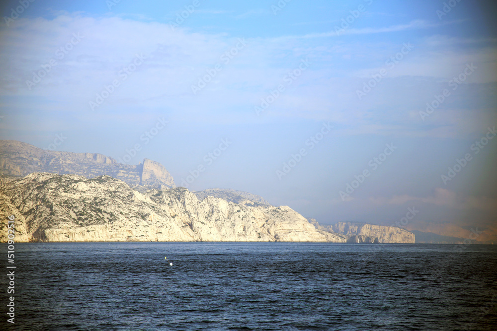 View of the high and steep rock face of the badlands on the Mediterranean sea, under a hazy sky, Parc National des Calanques, Marseille, France View of the high and steep rock face of the badlands on the Mediterranean sea, under a hazy sky, Parc National des Calanques, Marseille, France