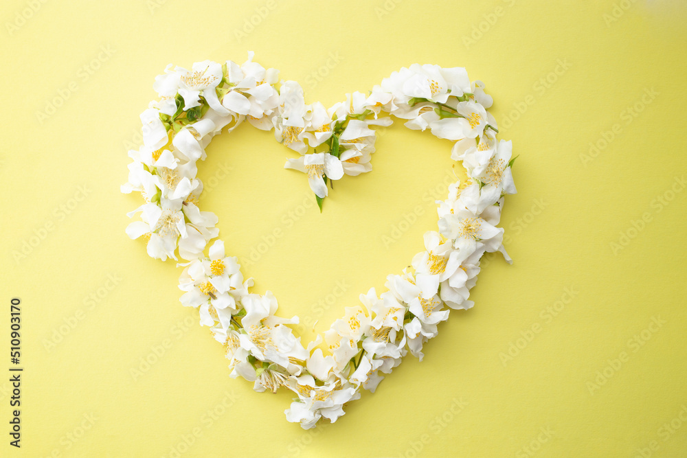 White little flowers frame in the shape of a heart on yellow background. Romantic card mockup, template or backdrop. 