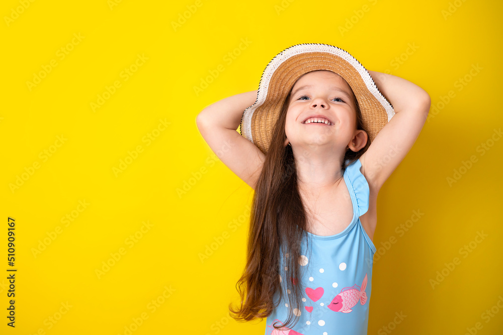 Summer vacation by the sea. Portrait of a cheerful girl in a blue swimsuit and hat on a colored yellow background. Space for text Summer vacation by the sea. Portrait of a cheerful girl in a blue swimsuit and hat on a colored yellow background. Space for text
