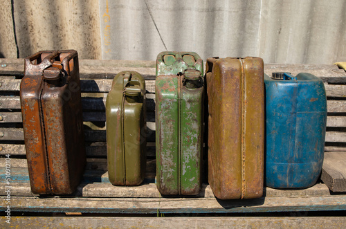 A group of old metal jerry cans with gasoline  stand on shelves in a wooden shed photo