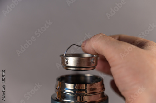 A man's hand takes the teapot out of the thermos. Silver brewpot and shiny threaded neck of modern thermos. Turquoise colored cylindrical vacuum flask. Container for hot and cold drinks. photo