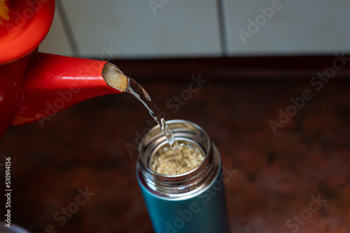 Boiling water from the red chanter is poured into a thermos. The teapot is filled with medicinal herbs. Dried flowers Matricaria chamomilla. Selective focus. Series part. photo