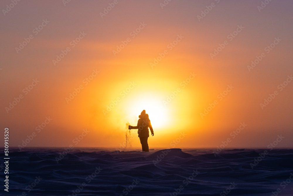 Beautiful arctic sunrise in northern Canada during peak wintertime. Woman silhouette standing in front of bright, blazing sun.	