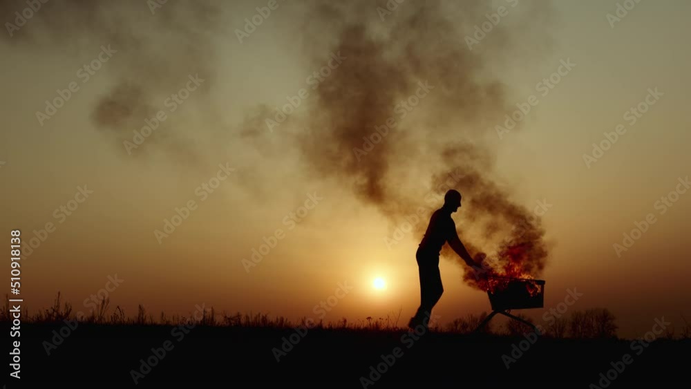 Wood Burning Inside A Shopping Cart In A Desolated City Homeless Area With A Corrugated Iron Sheet Leaning Against It As Windbreaker. Wood Burning Inside A Shopping Cart In A Desolated City Homeless Area With A Corrugated Iron Sheet Leaning Against It As Windbreaker.