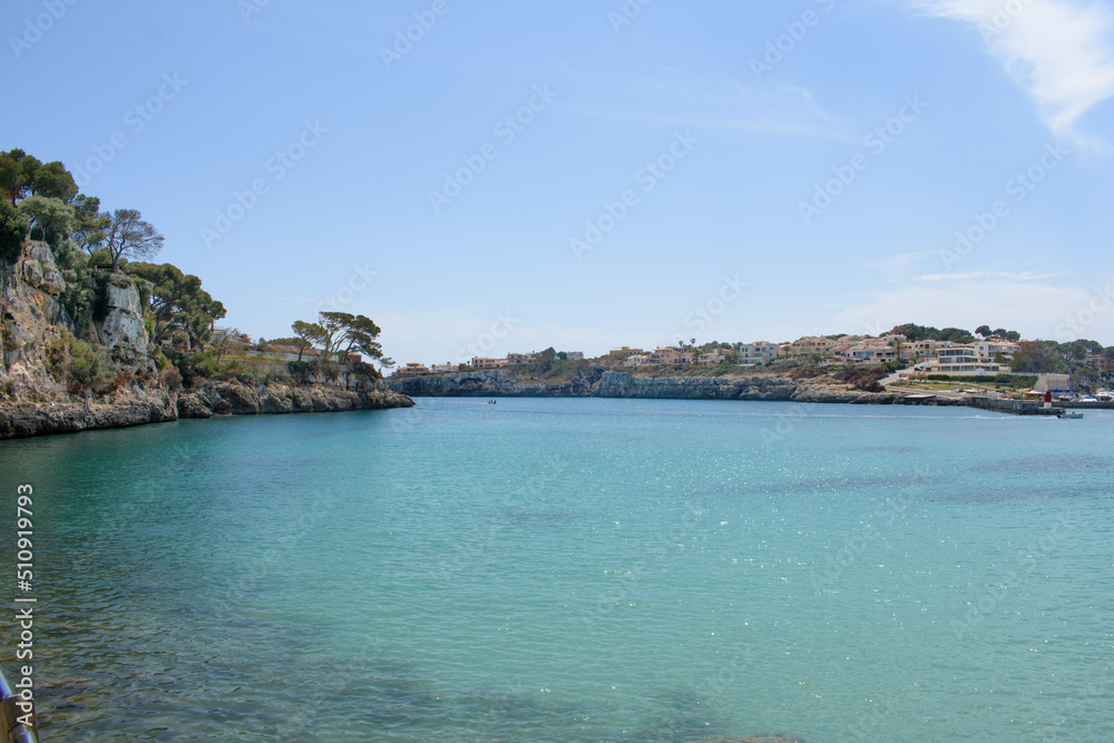 Naklejka premium Houses on top of the coastal cliffs in Porto Cristo. Calm, turquoise sea water.