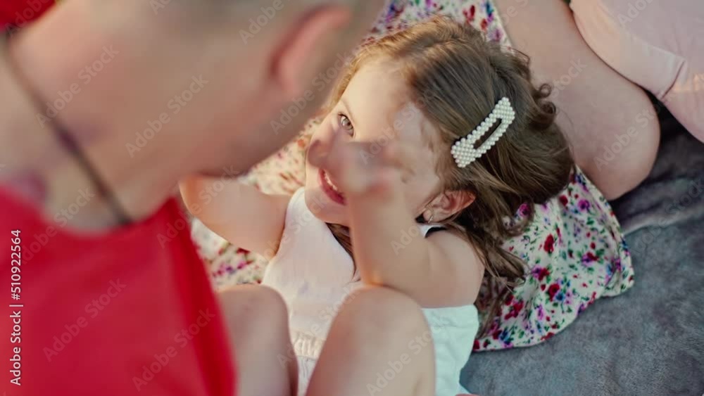 Young married couple with cute little daughter having fun together. A little daughter in a white summer dress lies on her mother's lap and laughs happily, parents play with the child .