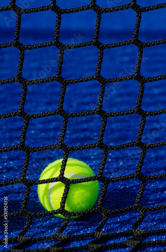 Selective focus, ball behind the net on a blue padel tennis court